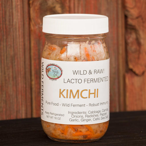 A glass jar of Wild & Raw Lacto Fermented Kimchi with a white lid and white label, set against a rustic wooden background.