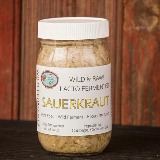 A jar of Sauerkraut, labeled 'Wild & Raw Lacto Fermented Sauerkraut', sitting on a dark wooden surface against a rustic reddish-brown wooden plank background.