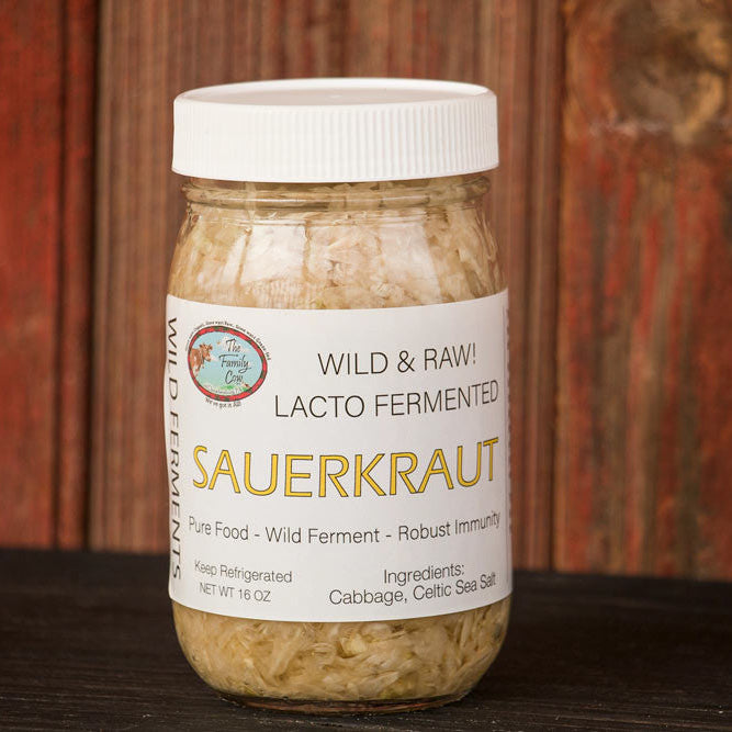 A jar of Sauerkraut, labeled 'Wild & Raw Lacto Fermented Sauerkraut', sitting on a dark wooden surface against a rustic reddish-brown wooden plank background.