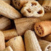 A pile of natural dried loofah or cucumber skin strips in warm tan and light brown tones, filling most of the frame against a white background.